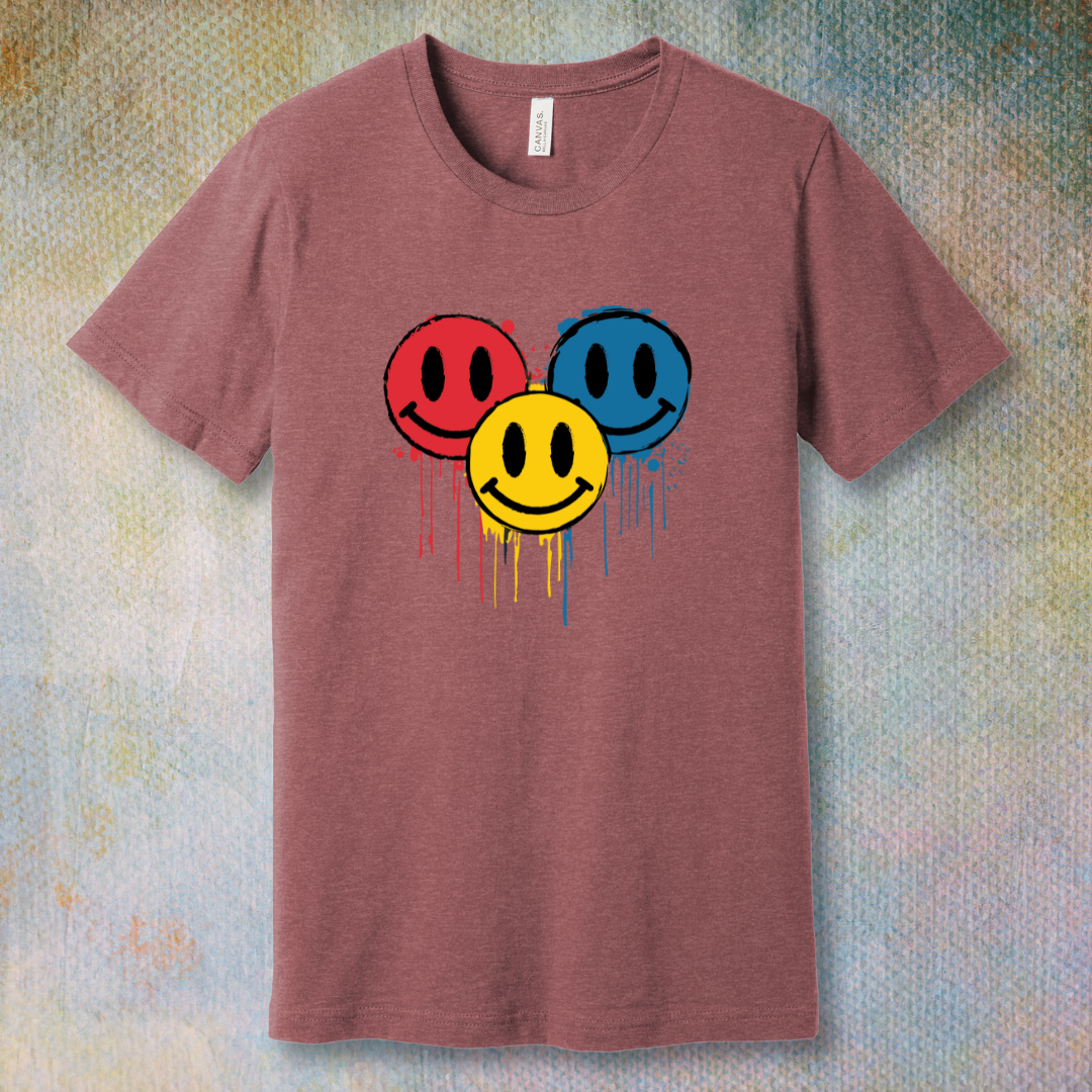 Drip Smile t-shirt — red, yellow, and blue smiley faces dripping paint on heather mauve tee