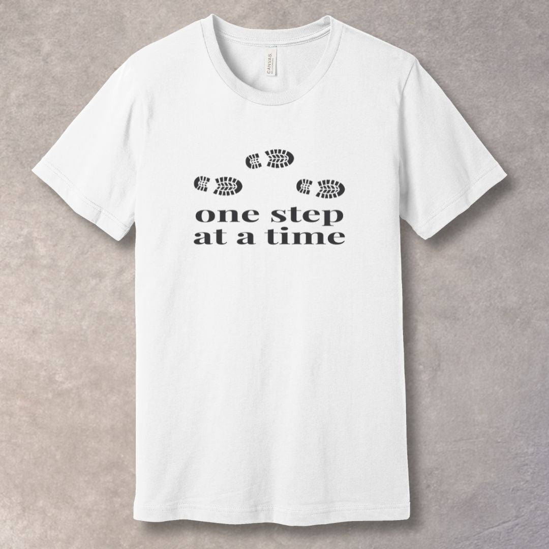 White t-shirt with 'one step at a time' text and footprints design